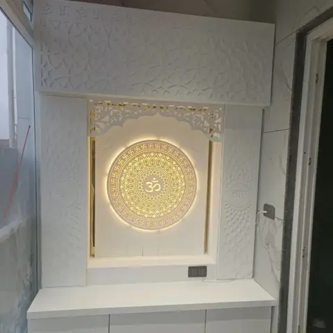 All-white CNC pooja unit with a Swastik-bordered backlit Om mandala, Shubh-Labh carved side panels and a drawer base