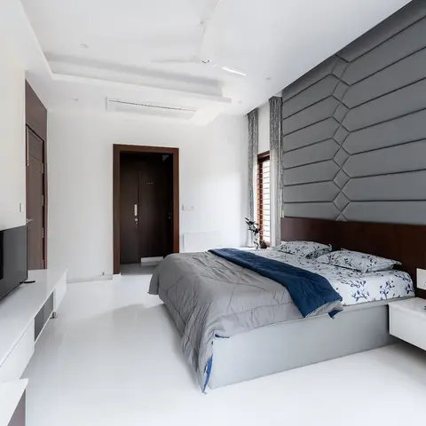 All-white minimalist bedroom with a grey chevron-channel upholstered headboard wall rising to the ceiling and a glossy white floor-to-ceiling TV console wall.