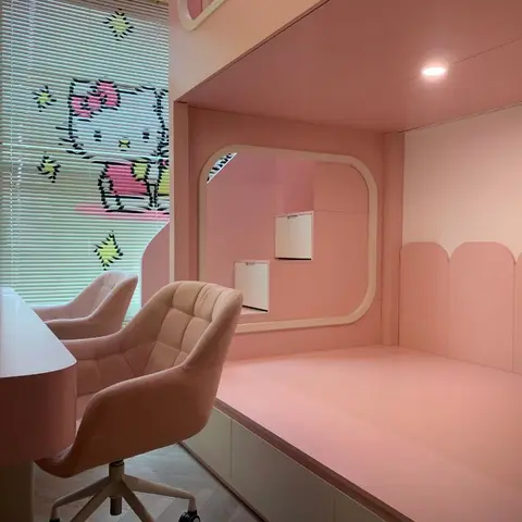 An all-pink children's room with a raised platform loft nook, a Hello Kitty window decal, and quilted blush pink upholstered chairs at a study desk