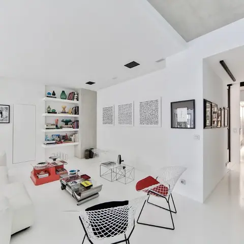 An all-white minimalist living room with a white sectional sofa, built-in white open shelving styled with books and objects