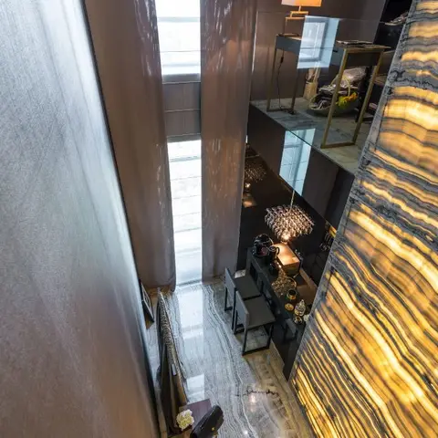 An angled overhead view into a double-height dining and bar nook with a backlit striped onyx feature wall, a glass-and-metal bar-height table with stools