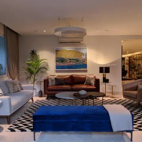 An eclectic living room mixing a brown leather sofa, grey linen sofa and blue velvet bench around nested round coffee tables on a black-and-white chevron rug.