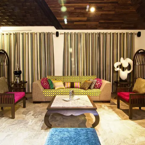 An eclectic living room with birdcage-shaped wooden armchairs in magenta velvet, a yellow geometric-print sofa