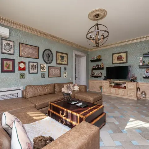 An eclectic living room with teal damask wallpaper, a gallery wall of vintage-style frames, a brown leather sectional around an ornate trunk coffee table