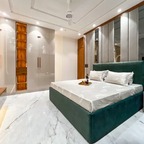 An emerald velvet bed on a white marble floor faces a run of ivory high-gloss wardrobes split by a backlit teak open-shelf column