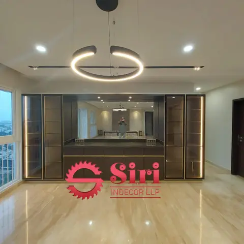 An empty living-dining space with a floor-to-ceiling black-and-gold bar unit, mirrored backsplash, and a ring pendant light above a beige marble floor.