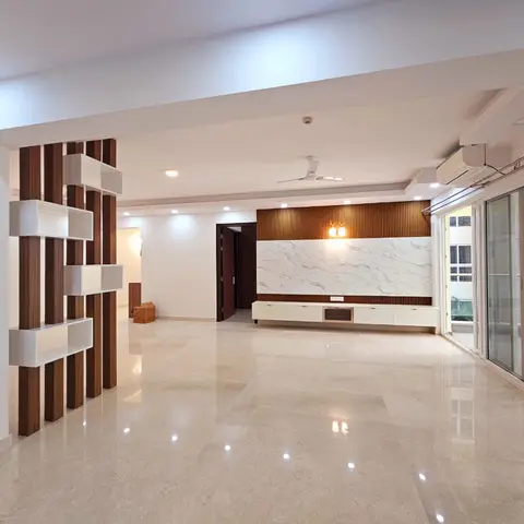 An empty living room with a marble-and-wood-fluted TV feature wall, a floating white console, and a decorative partition shelving unit, opening to a balcony.