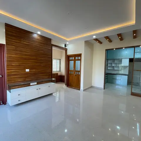 An empty living room with a book-matched wood-veneer TV feature wall, a white console with a glass display shelf, a warm cove-lit ceiling