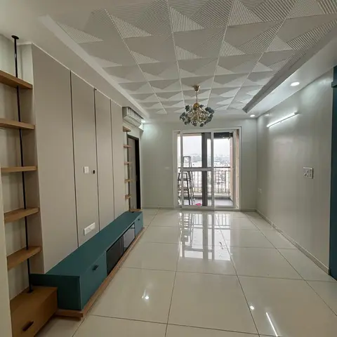 An empty living room with a 3D triangular geometric POP false ceiling, a floral pendant chandelier, and a teal TV console against a grey wall.