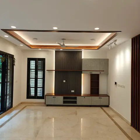 An empty living room with a fluted-panel TV wall flanked by grey cabinetry, a wood-trimmed cove ceiling, and inlay-bordered marble flooring.
