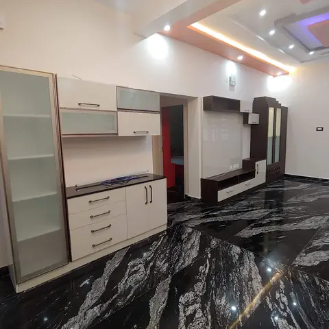 An empty living room with dramatic black-and-white veined granite flooring, a built-in wood-finish TV unit and matching cabinet