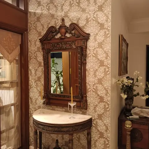 An entrance corner with a demilune marble-top console table below an ornately carved wood mirror, set against a gold-and-cream damask wallpaper