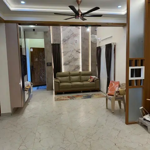An entrance-facing living room with a backlit marble feature wall between the seating area and a carved wooden front door, an olive leather sofa