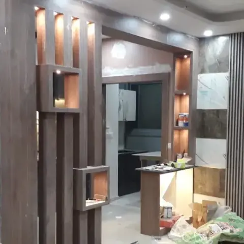 An entrance foyer under construction with a slatted wood jaali partition holding lit display niches