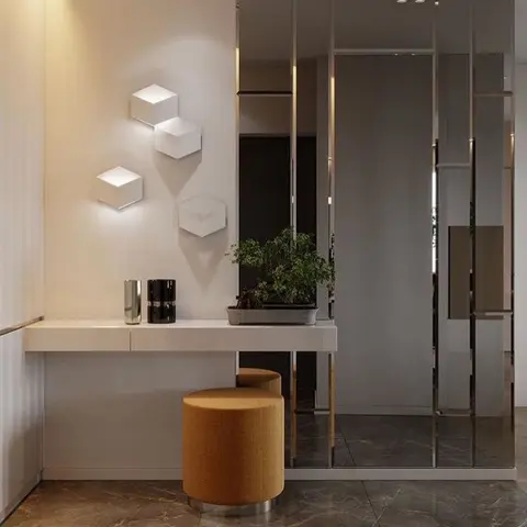 An entrance foyer with a floating console table, cube-shaped wall sconces, a mustard ottoman, and a mirrored panel partition wall.