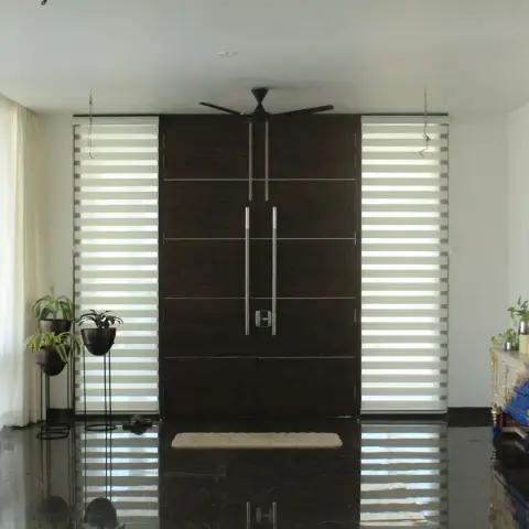 An entrance foyer with a tall dark wood double front door flanked by striped zebra blinds, a glossy black marble floor