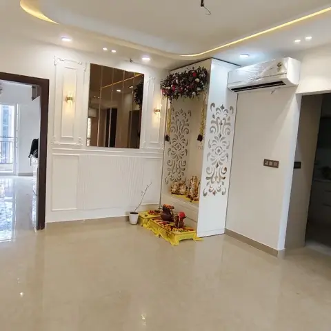 An entrance foyer with a wainscoted mirror wall panel and wall sconces, opening to a built-in white jaali-panel pooja niche with a floral garland.