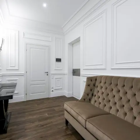 An entrance foyer with full-height white classical wall panelling and moulding, a dark wood floor
