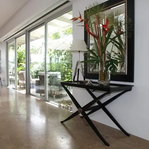 An entrance hallway with a black X-frame console table styled with a tall floral arrangement beneath a large black-framed mirror