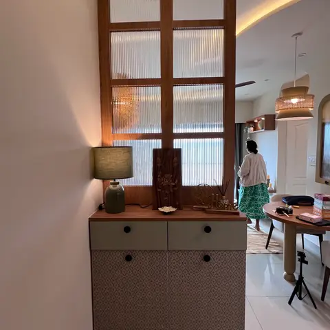An entrance nook with a reeded-glass framed wood partition door, a console table styled with a ceramic lamp and wood carving