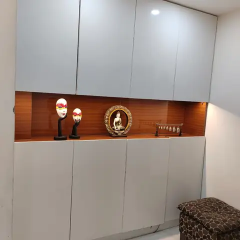 An entrance storage wall with white lacquered cabinets flanking a backlit wood-panel display niche styled with Balinese face masks
