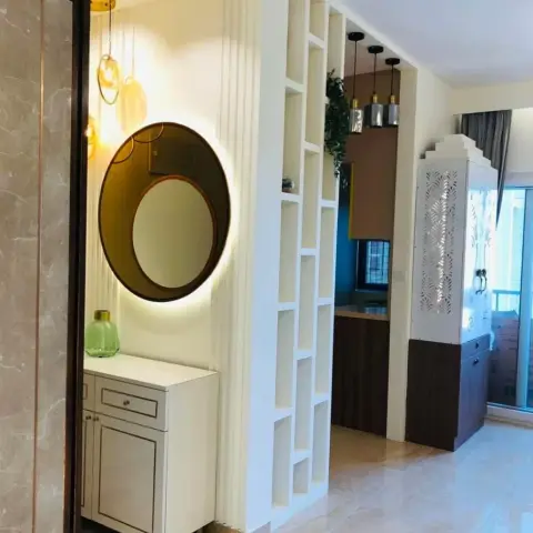 An entry vignette with an ivory drawer console under a backlit round mirror in a wooden ring, set on fluted panelling with amber glass pendants overhead