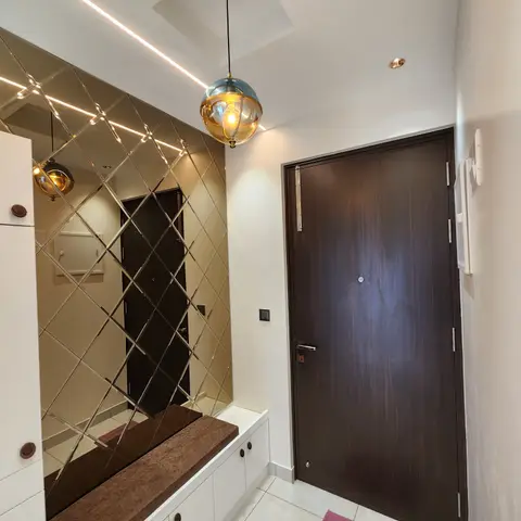 An entryway with a diamond-cut mirror tile accent wall, a built-in bench with storage cabinets, and a globe pendant light beside the dark wood main door.