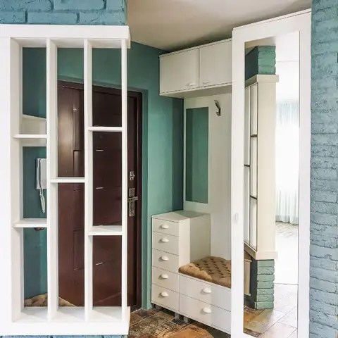 An entryway with exposed teal-painted brick walls, a white shoe cabinet with a tufted bench seat, and a full-length mirrored wardrobe beside the main door.