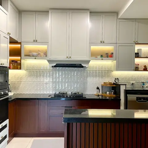 An L-shaped kitchen with white shaker upper cabinets over dark wood lower cabinets, a backlit ribbed-glass backsplash
