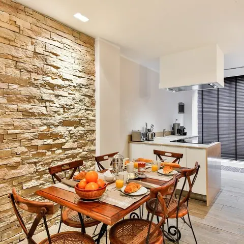 An open dining nook with a rustic wood table set for breakfast against a stacked stone accent wall, opening into a compact white kitchen counter and hood.