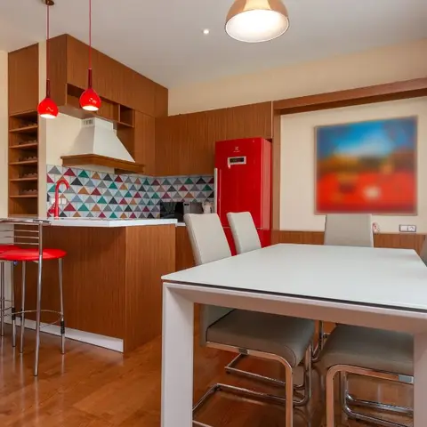 An open kitchen and dining space with a colorful triangle-mosaic backsplash, a glass block feature wall, a red retro fridge and a white dining table for six.