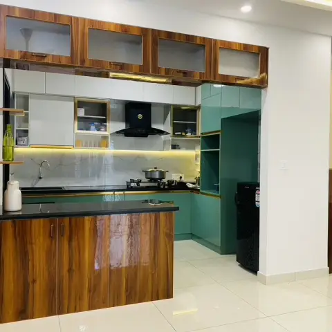 An open kitchen seen from the dining, closed off by a walnut high-gloss pass-through counter, with teal-green gloss base and tall units edged in gold profile