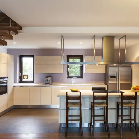 An open kitchen with a waterfall-edge island and dark wood bar stools, suspended overhead cabinetry, integrated stainless appliances