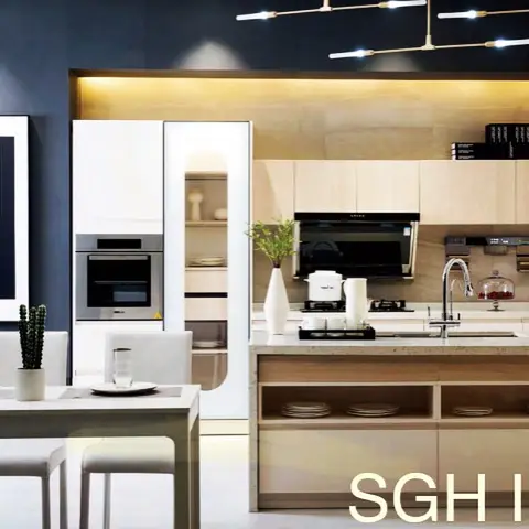 An open kitchen with light wood cabinetry and a built-in oven tower beside a dining table, lit by a branching pendant fixture against a navy accent wall.
