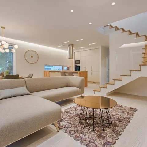 An open living area with a large grey sectional sofa and a mirrored-top wire-base coffee table on a circular patterned rug