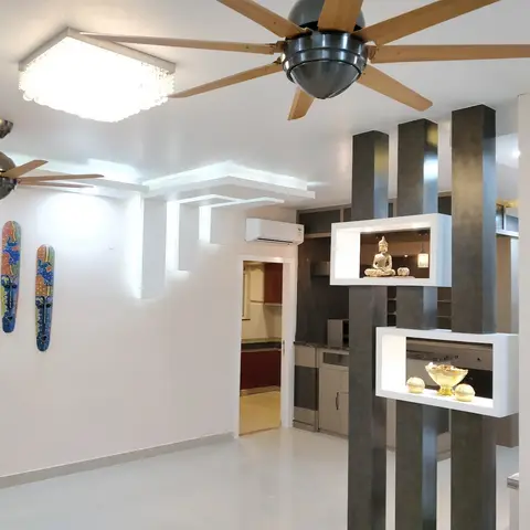 An open living space with a stepped cove ceiling and a fluted room-divider column holding white display niches with a Buddha statue
