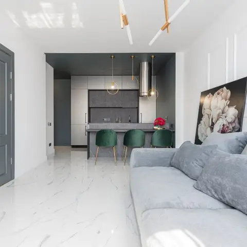 An open living space with a grey velvet sectional sofa, a floral art print leaning against a panelled wall