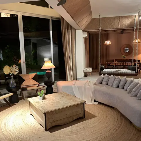 An open lounge with a curved grey sofa and woven rope armchairs around a wooden trunk coffee table on a round jute rug