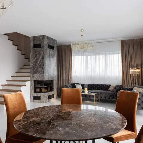 An open-plan dining and living space with a round marble dining table and mustard velvet chairs in the foreground