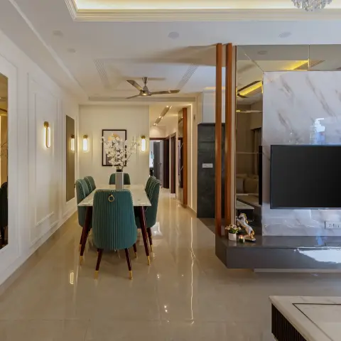 An open-plan hallway showing a green channel-tufted velvet dining set on a marble table beside a marble-clad TV feature wall framed by vertical wood slats.