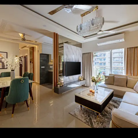 An open-plan high-rise living-dining space with teal velvet dining chairs at a marble table on one side and a cream L-shaped sofa facing a wall-mounted TV on