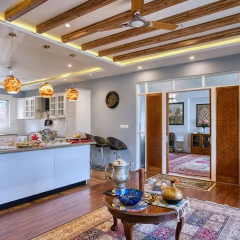 An open-plan kitchen and living space with an exposed wood beam ceiling, three amber glass pendant lights over a white kitchen island