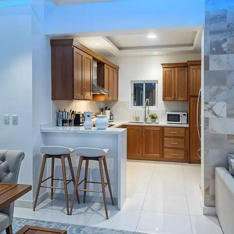 An open-plan kitchen, dining and living space with cherry-wood kitchen cabinets, a marble breakfast bar with leather stools, a patchwork marble accent wall