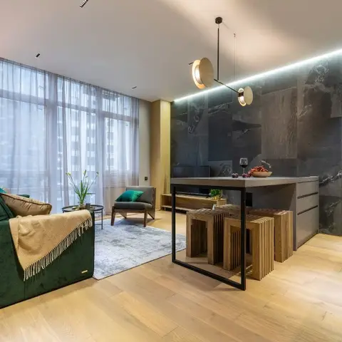 An open-plan living-and-dining space with a dark green velvet sofa opposite a floor-to-ceiling stone-clad wall