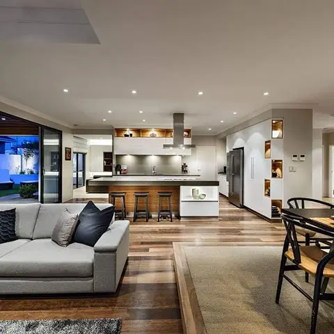 An open-plan living-kitchen-dining space with a grey sofa in the foreground, a white waterfall-edge kitchen island with bar stools