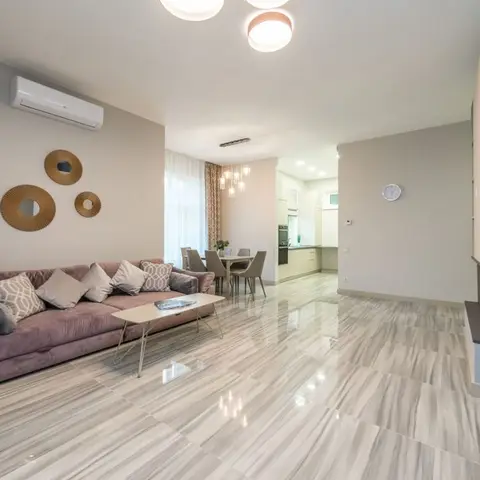 An open-plan living room with a mauve velvet sofa, a cluster of three round sunburst mirrors on the wall, and a dining table and kitchen visible beyond.