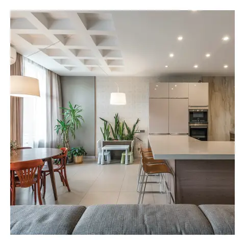An open-plan space with a coffered grid ceiling, a round wood dining table with bentwood chairs, a kids' play corner