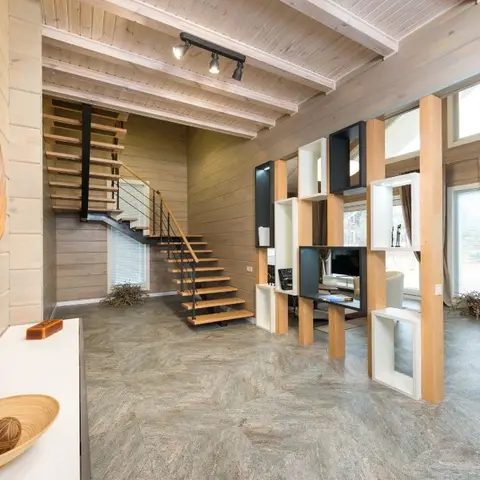 An open-plan wood-clad home interior with a floating wood-and-black staircase and a cube-shelf partition dividing the entry from the living area beyond.