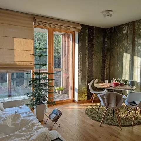 An open studio space with a forest-mural accent wall behind a round dining table and white chairs on a round rug