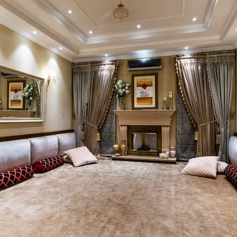 An ornate floor-seating majlis-style room with low bench seating and red patterned bolster cushions around the walls